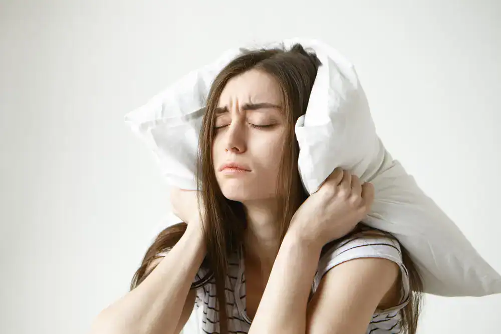 a female is in sleepless state, covering her head with a pillow 